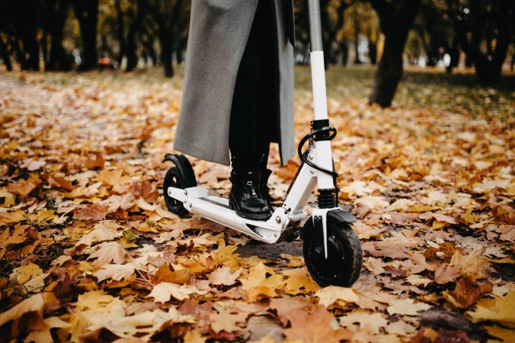 Femme sur une trottinette électrique, en forêt sur des feuilles