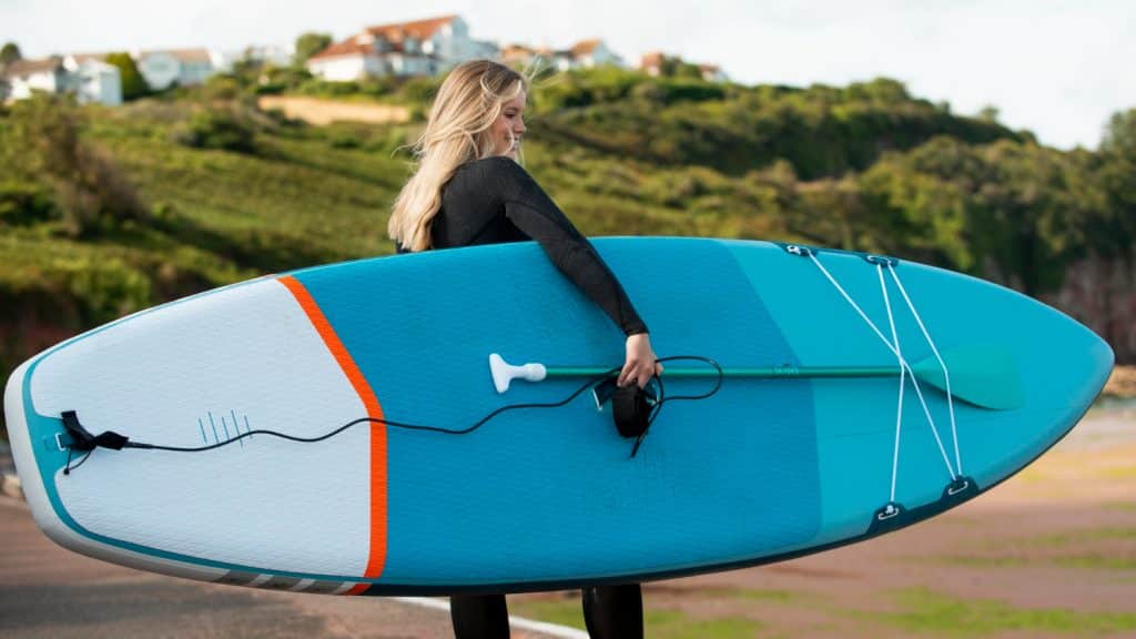 Femme tenant une planche de paddle et un rame sur la plage
