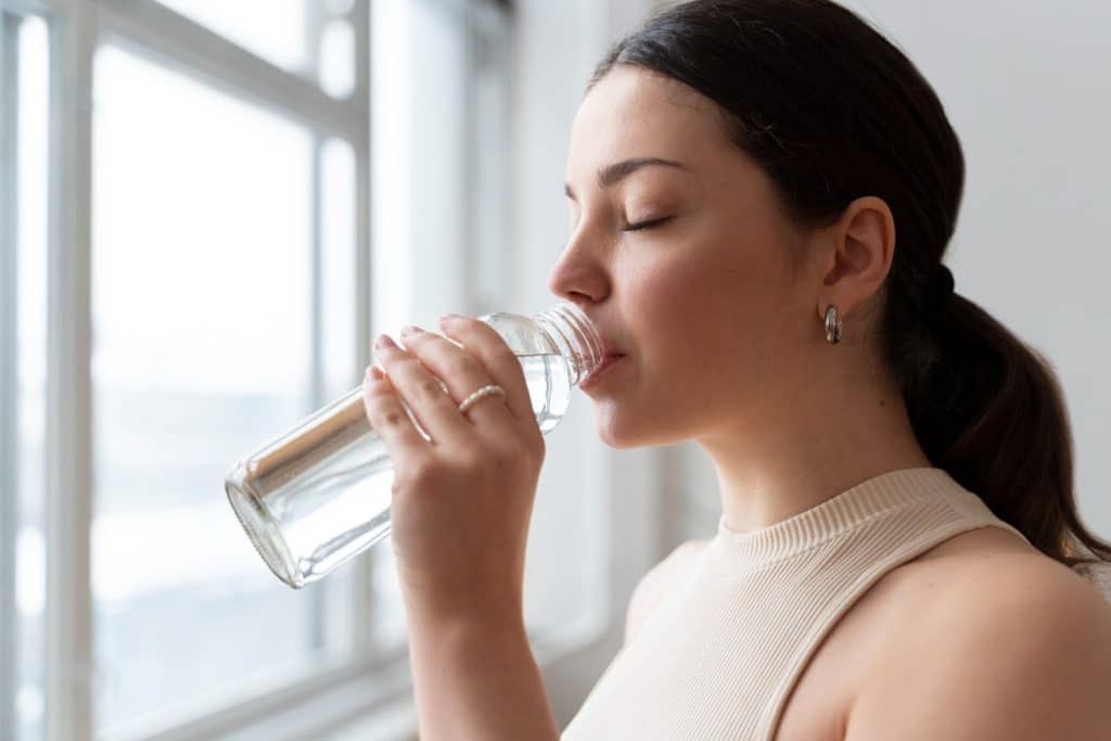 Femme buvant devant une fenêtre dans une bouteille d'eau